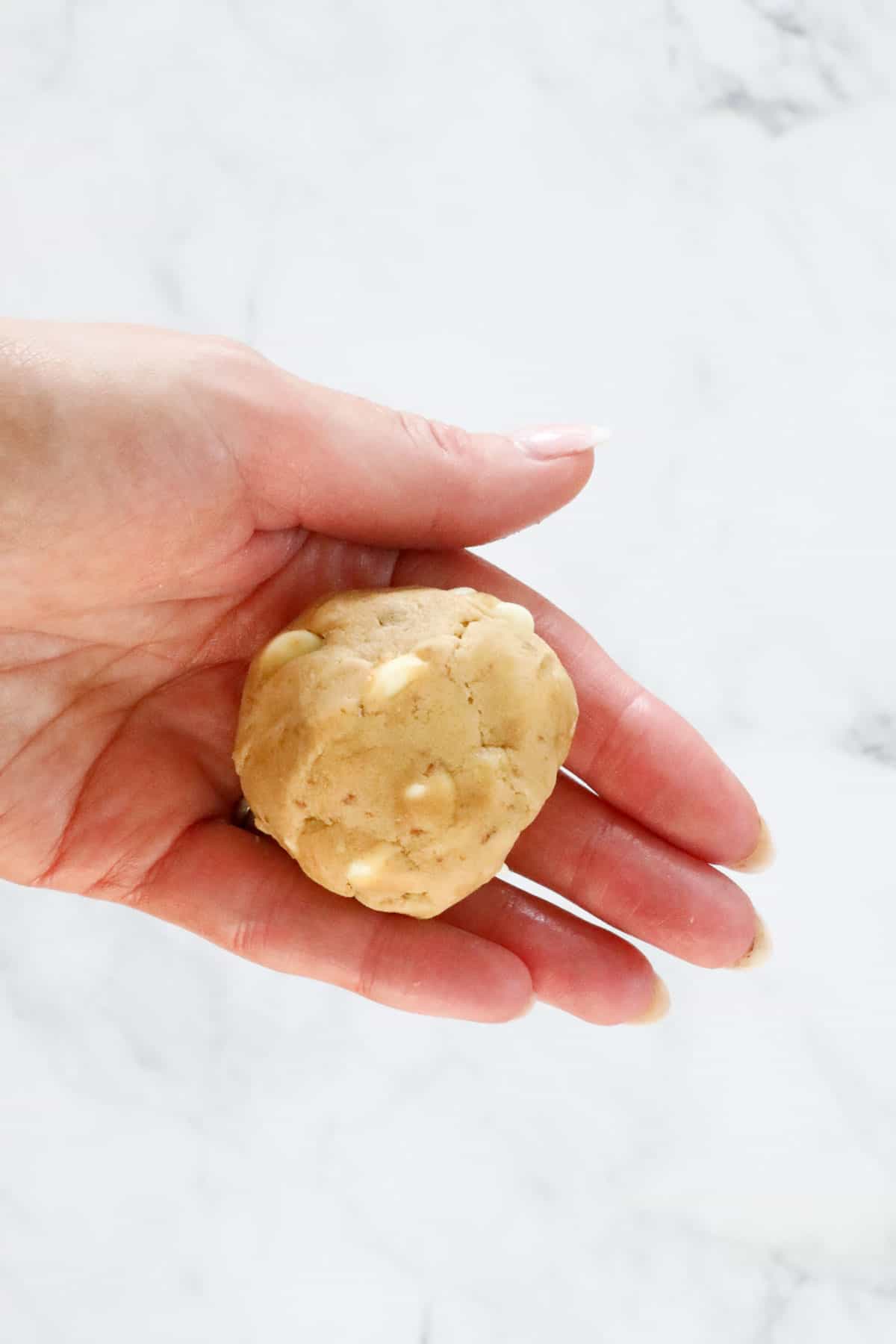 A hand holding a ball of cookie dough, encasing Biscoff spread inside.