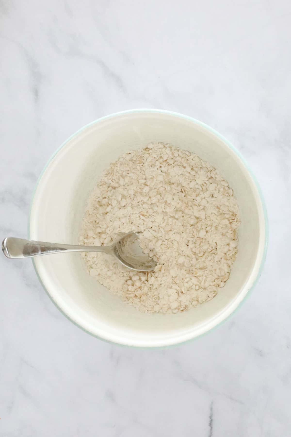 Flour, rolled oats, bicarb of soda and sugars in a white mixing bowl.