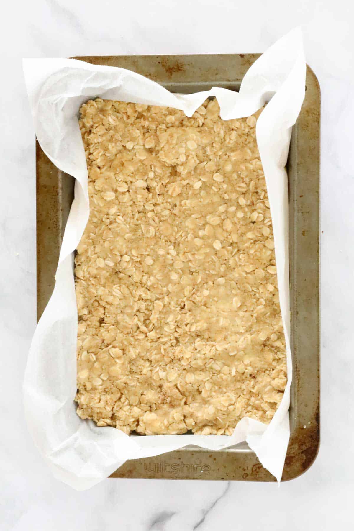 Half the crumble mix pressed into a paper lined slice tray.