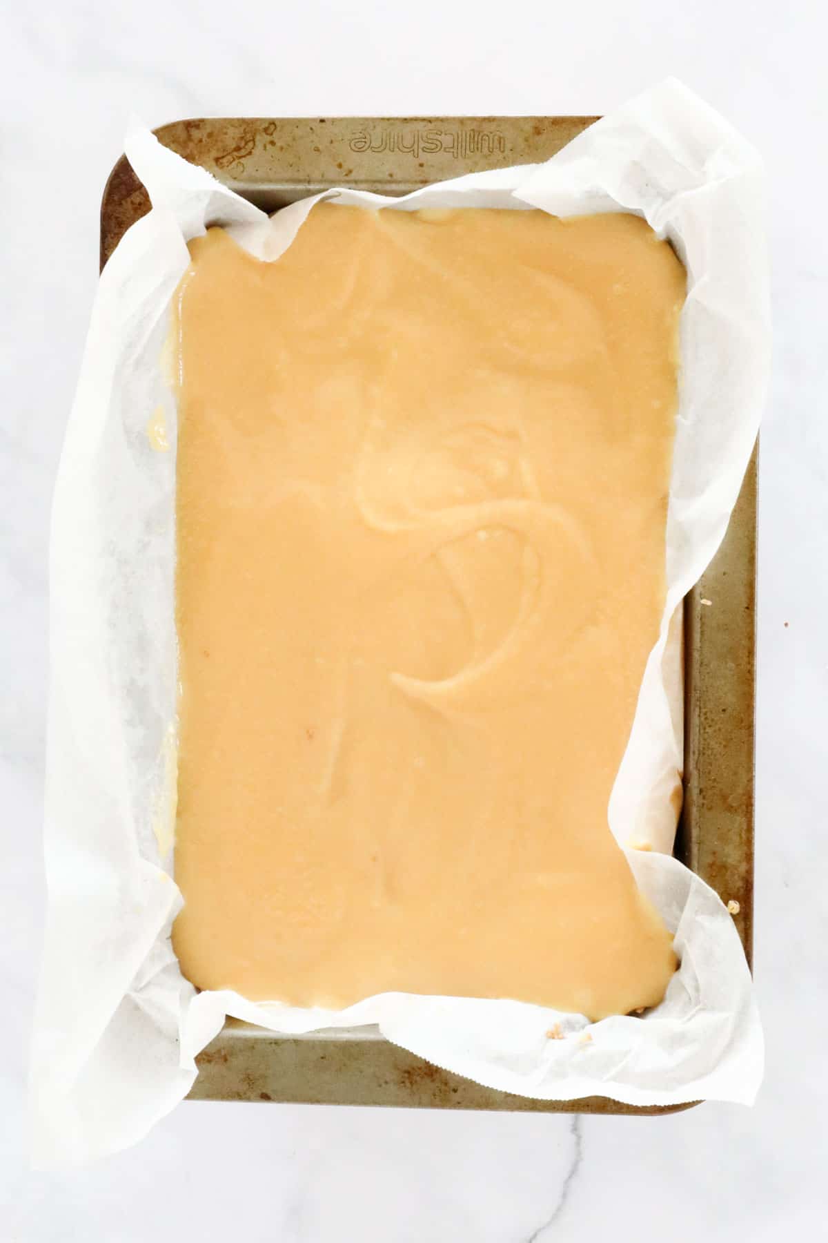 Thick caramel mix poured over baked base in a baking tray.