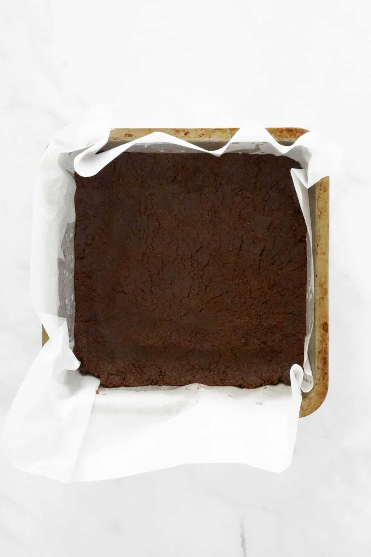 The chocolate biscuit base pressed into a lined square tin.