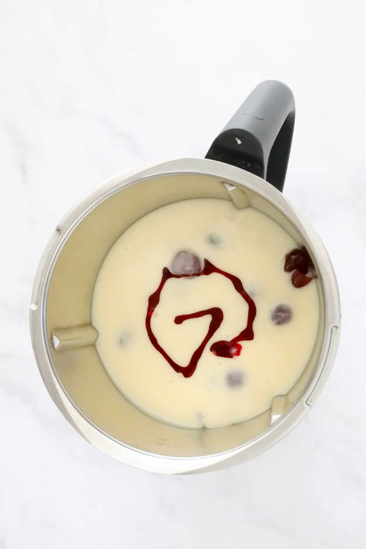 Condensed milk, coconut, glace cherries and red food colouring in the bowl of a Thermomix.