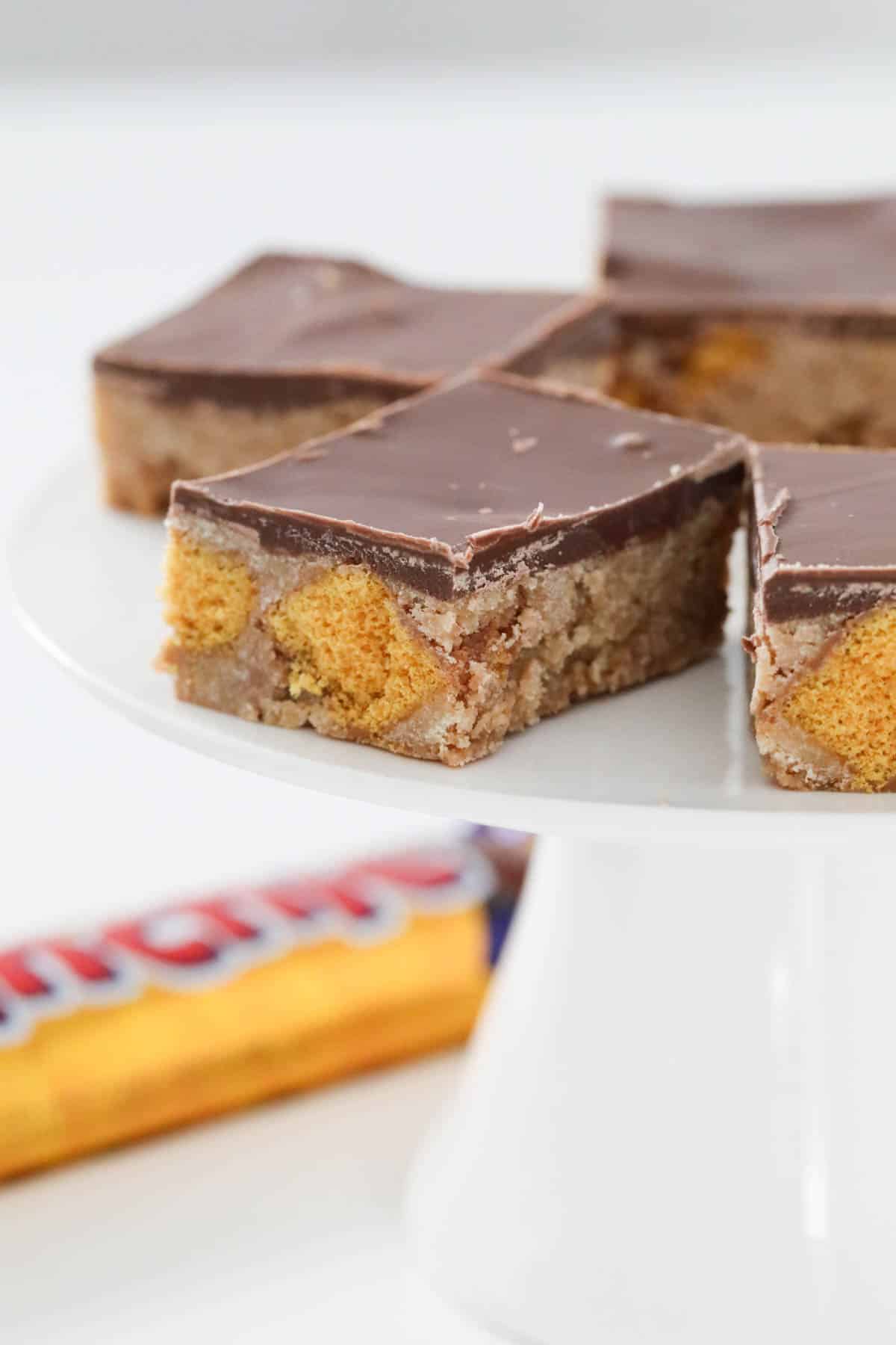 Honeycomb slice on a cake stand with a Crunchie bar behind.