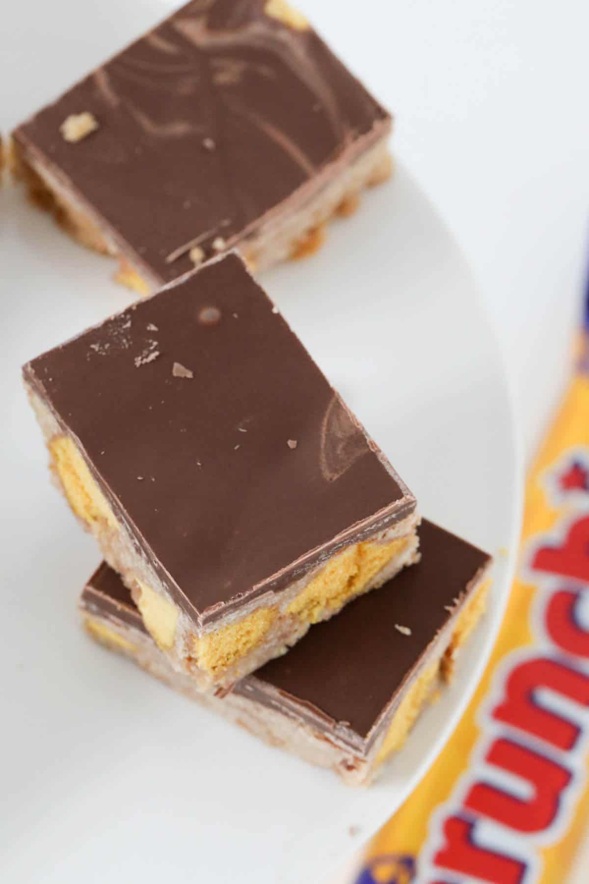 An overhead shot of squares of a chocolate topped slice filled with chunks of Crunchie bars.