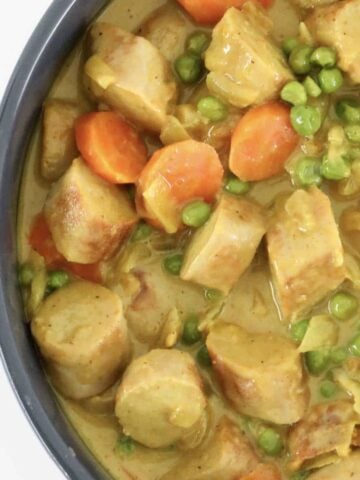 An overhead shot of curried sausages with peas and carrots.