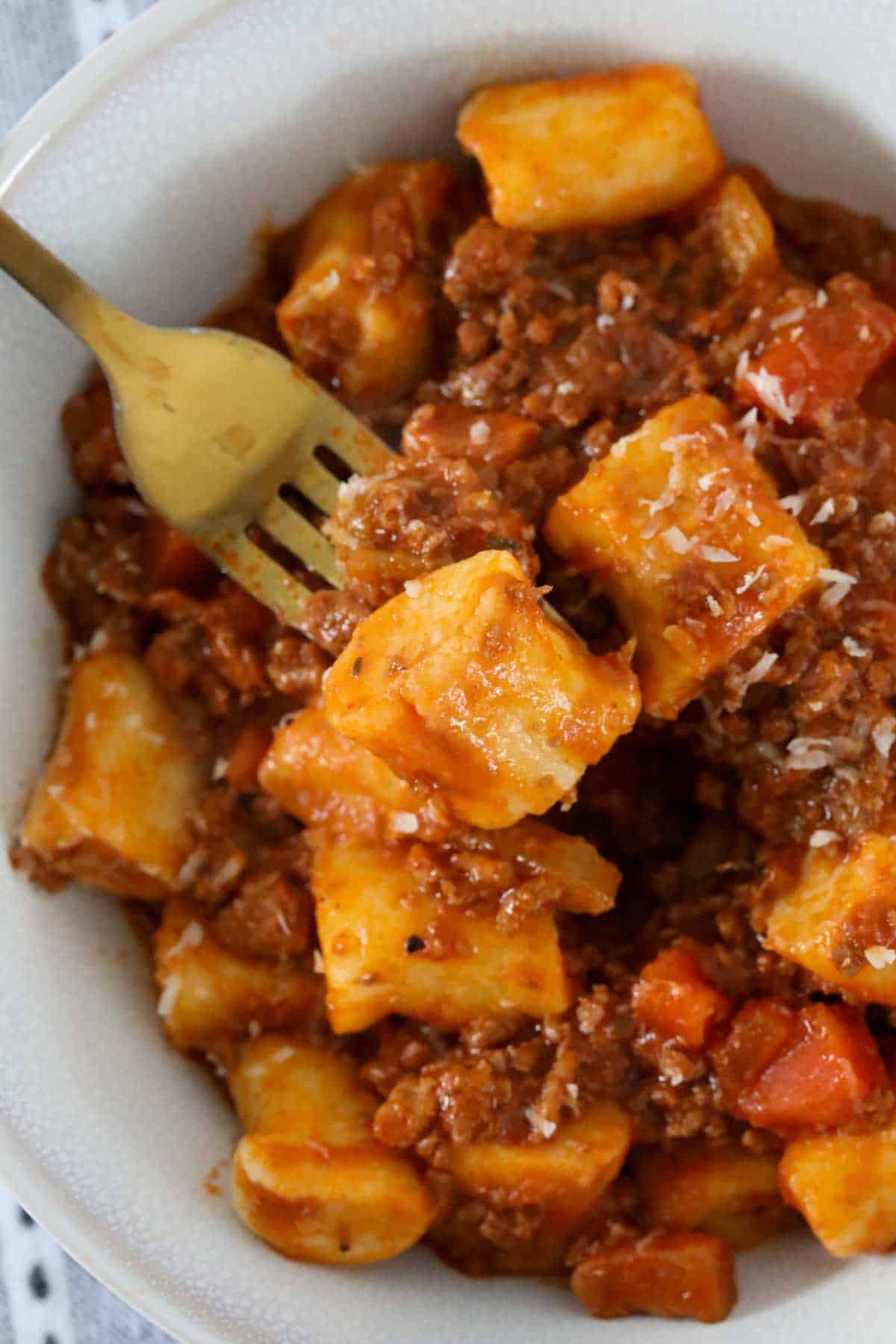 Gnocchi served with bolognese sauce being eaten with a fork.