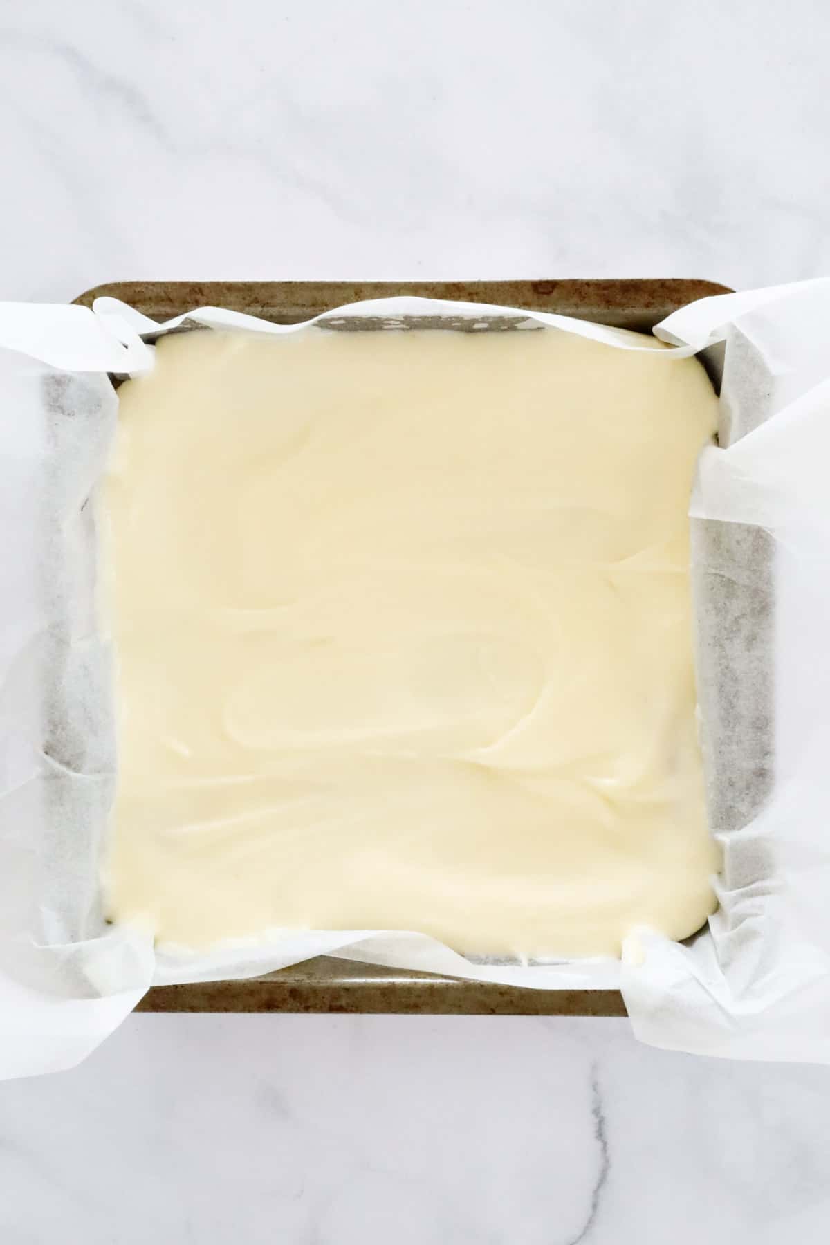 Lemon frosting spread over baked base in a lined baking tin.