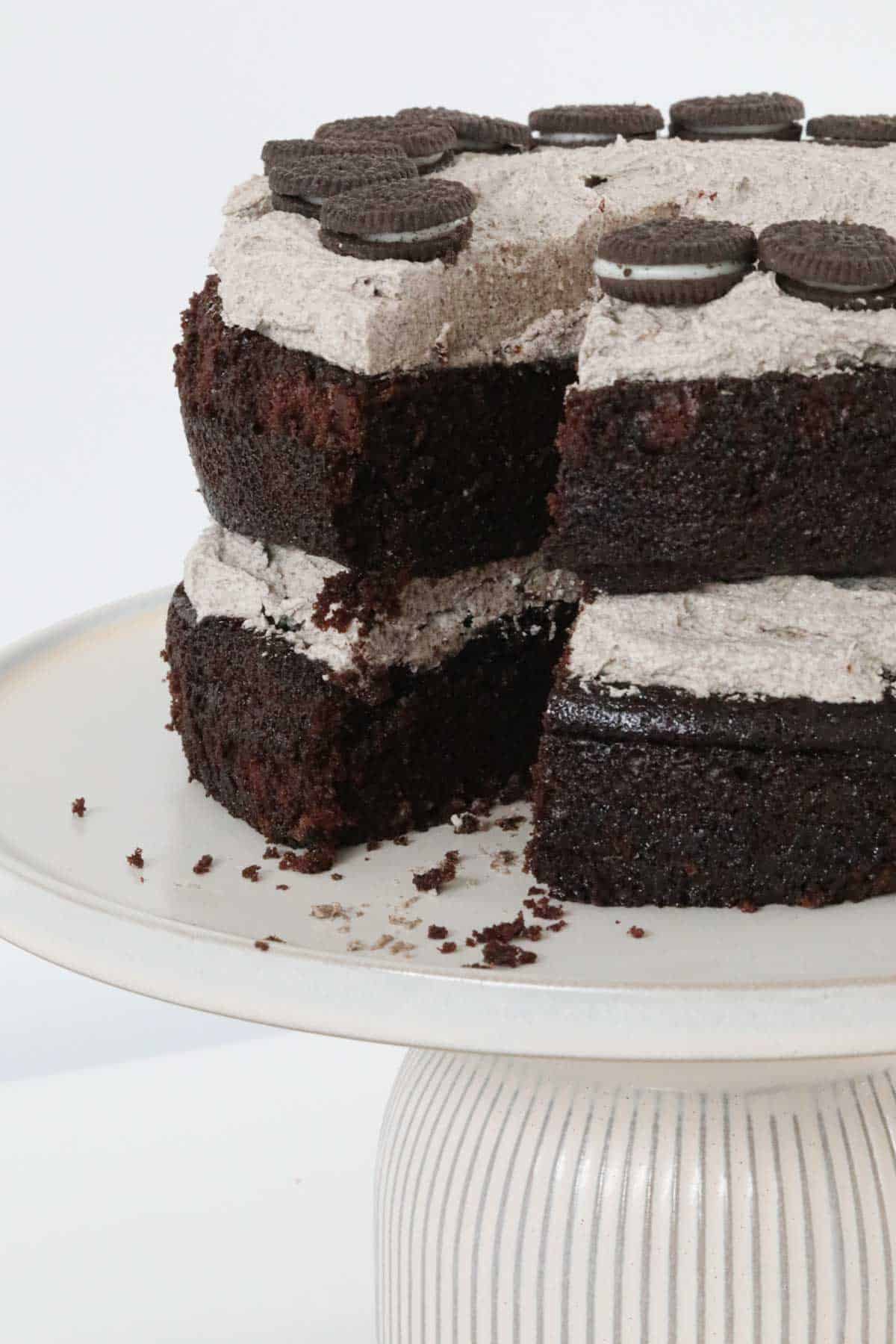 A rich cookies and cream mud cake with one slice removed, on a white cake stand.