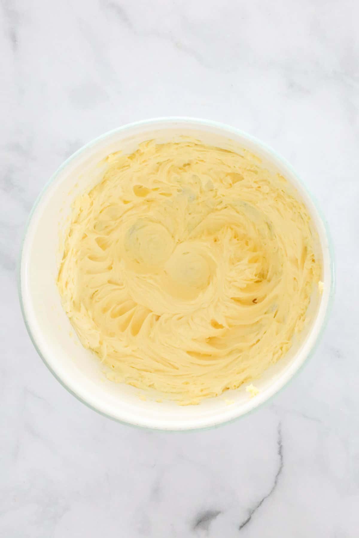 Soft beaten butter in a white mixing bowl.