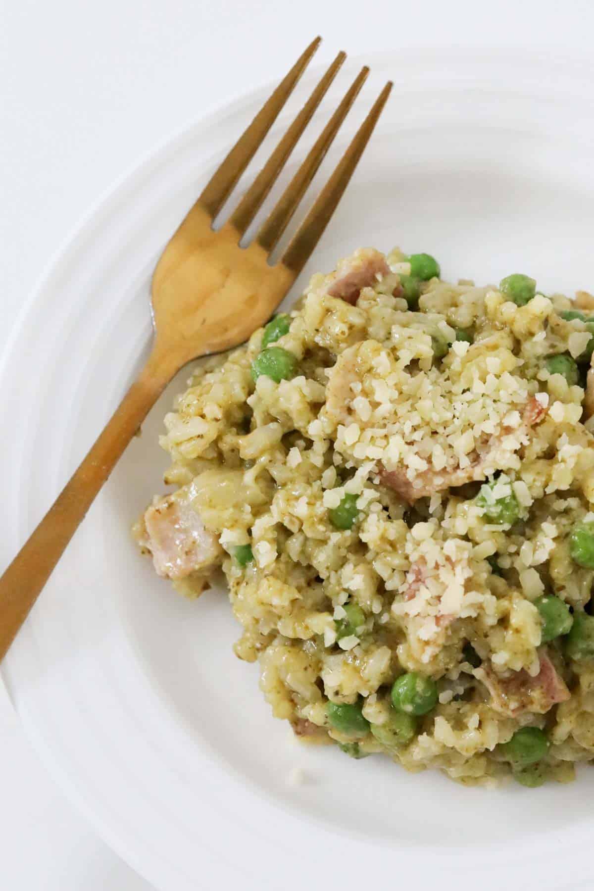 Bacon, pea and pesto risotto on a white plate, with a fork to the side.