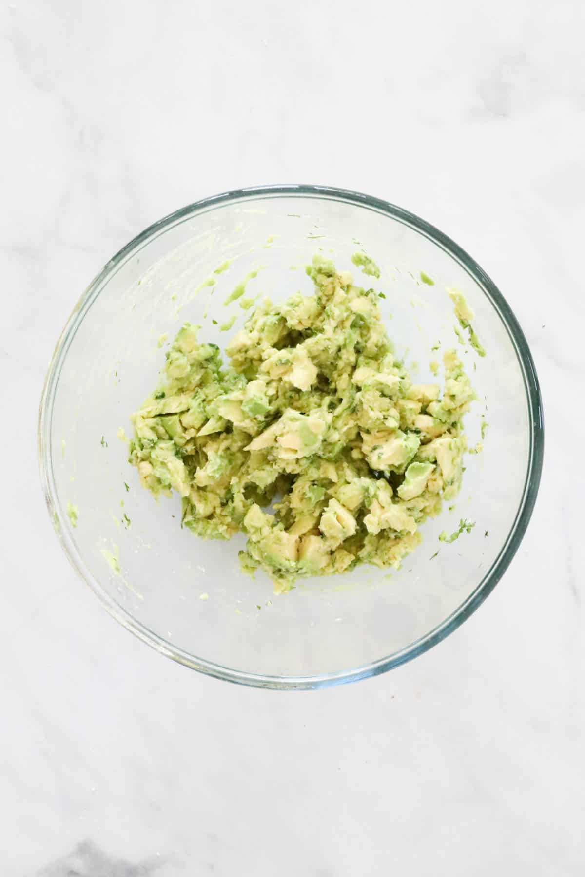 Chunks of avocado and herbs in a bowl.