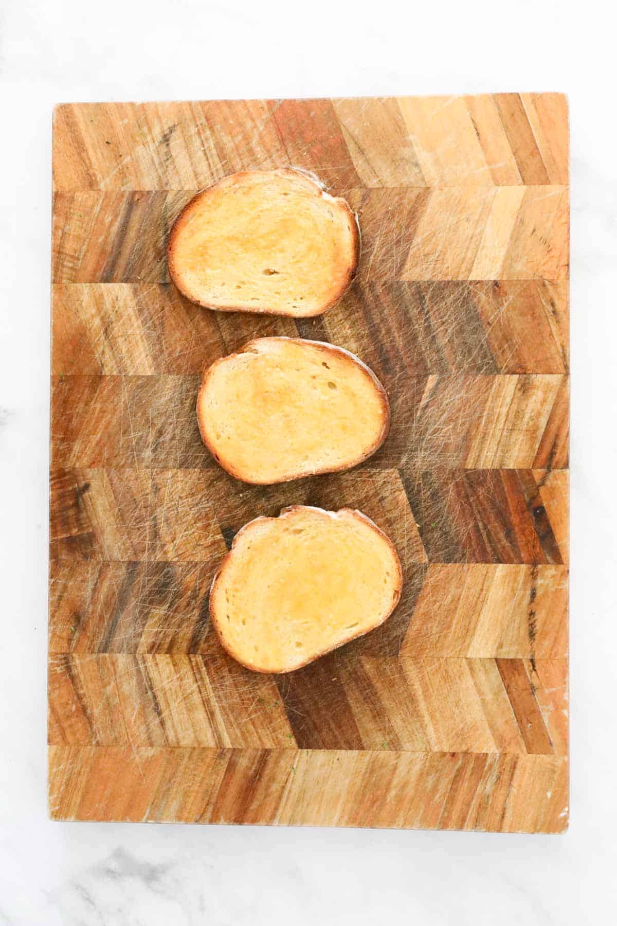 Three slices of toasted sourdough, buttered, on a wooden board.