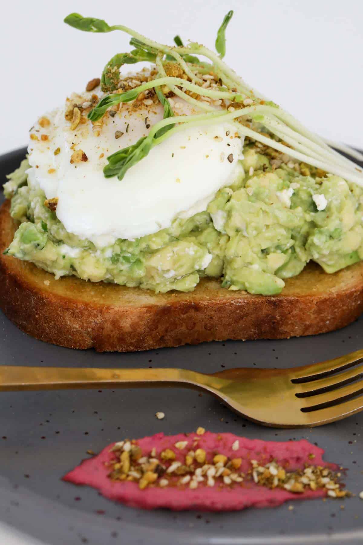 Side view of avo on toast, topped with a poached egg, with dukkah and beetroot dip on the side.