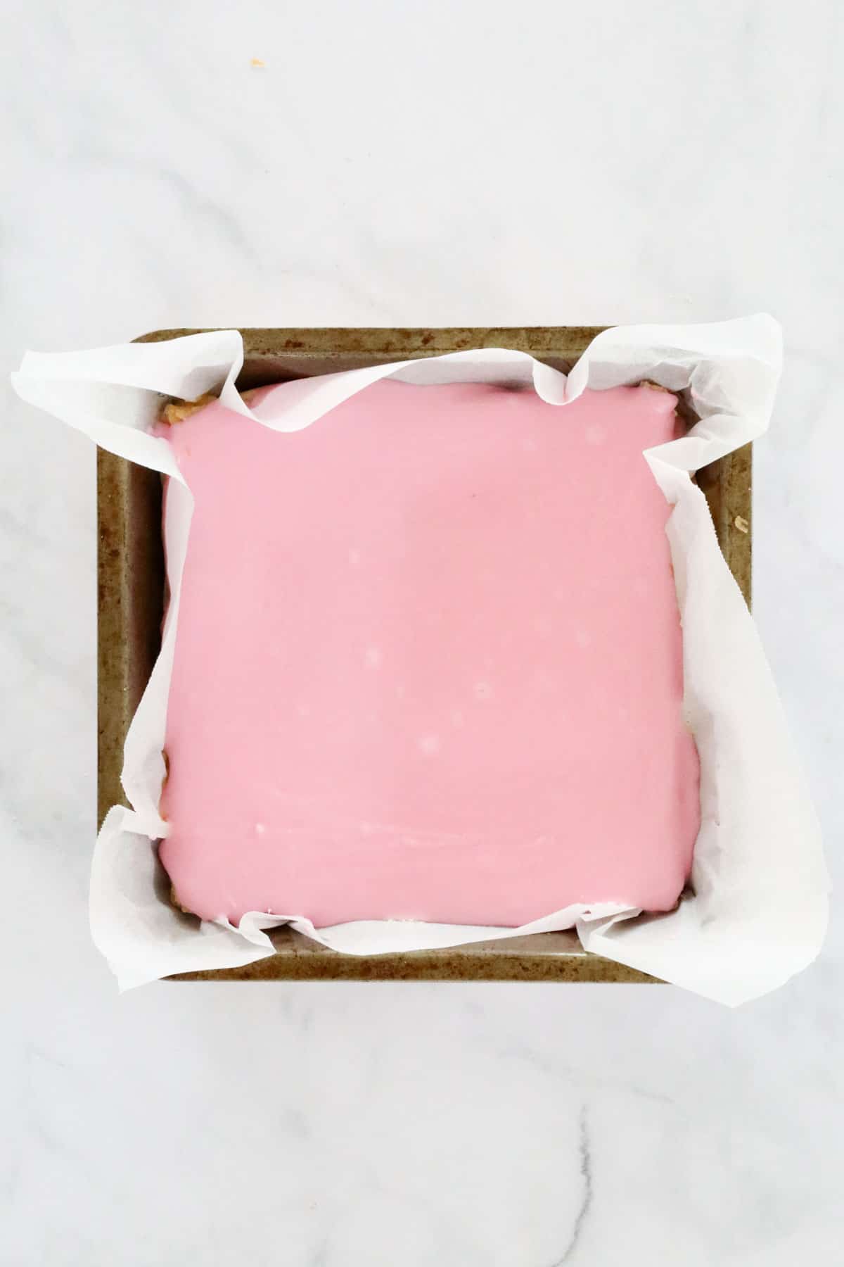 Pink glaze spread over the top layer of baked puff pastry in a paper lined tin.