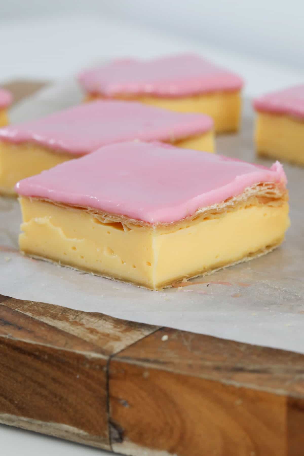Vanilla Custard Slice with a pink glaze, cut into squares on baking paper.