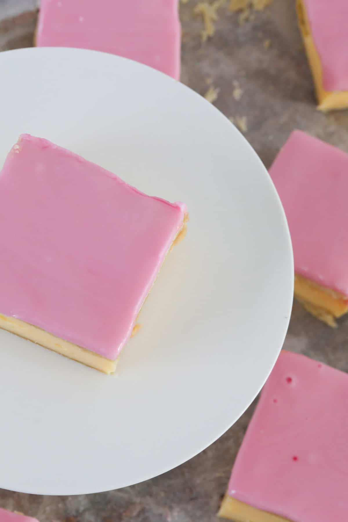 Looking down on pink glaze on top of a vanilla custard slice served on a white plate.