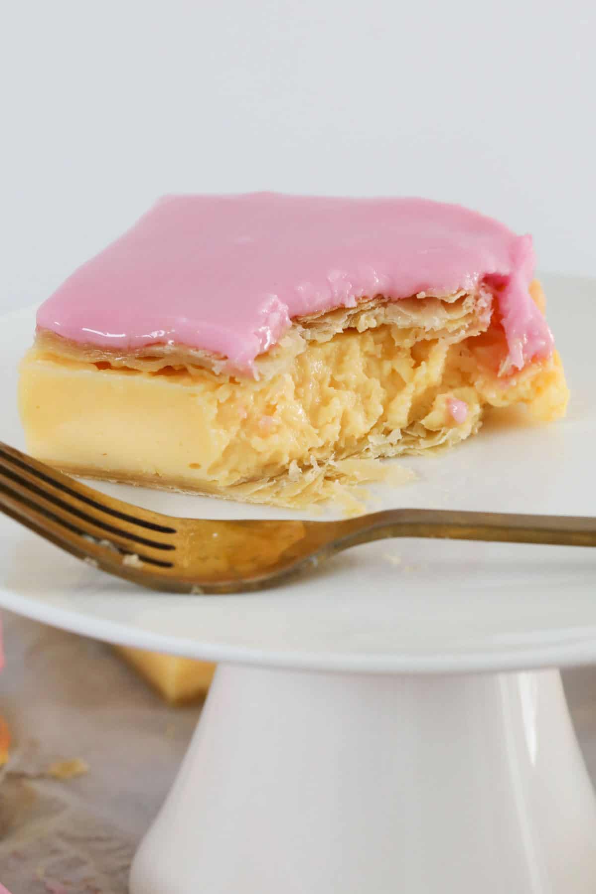 A close up of a piece of vanilla custard slice served, with a forkful removed and the fork resting beside.