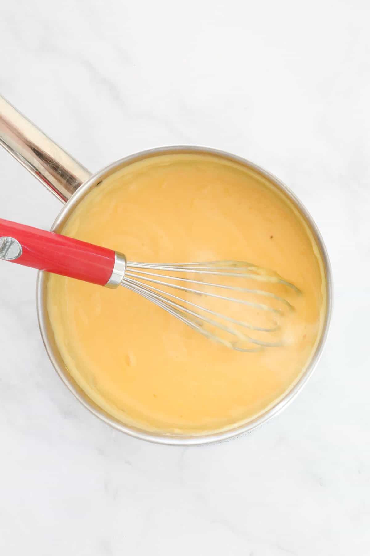 Thickened custard powder in a pot with a red handled whisk.