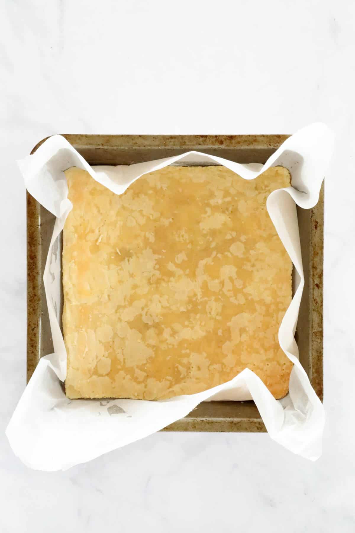 A sheet of baked puff pastry placed on the base of a square lined baking tin.