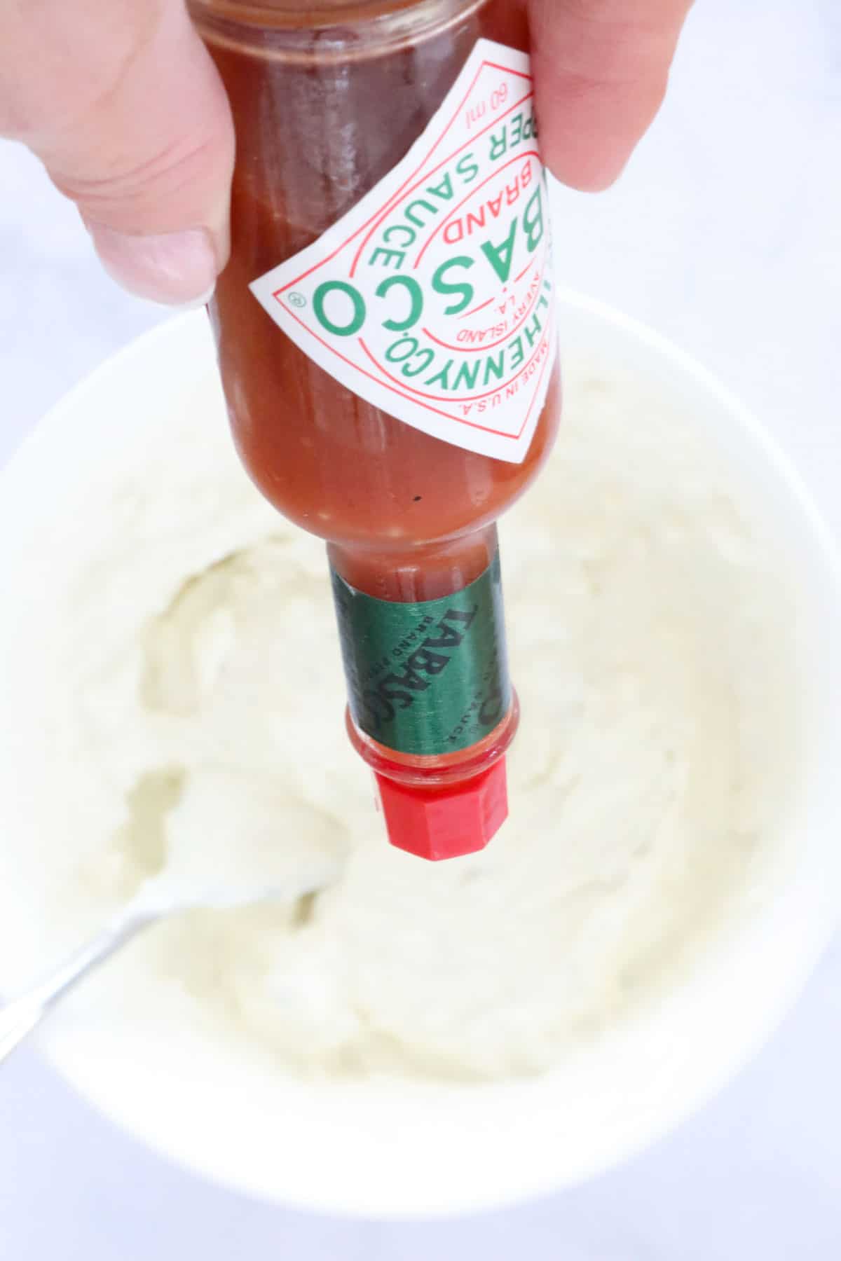 A bottle of Tabasco held upside down over the mixing bowl.