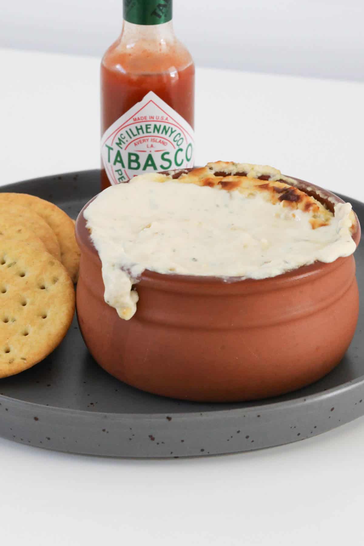 A bottle of Tabasco behind a ramekin filled with warm blue cheese dip.