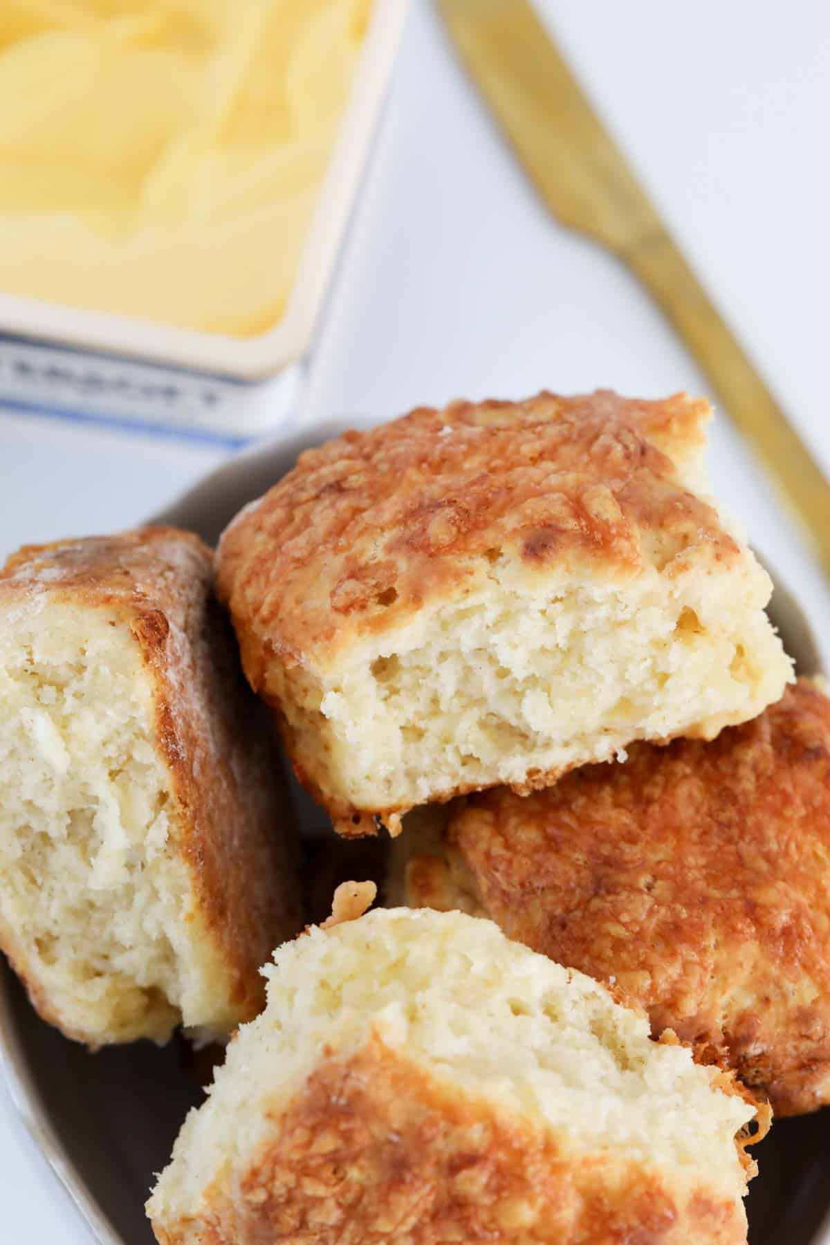 A batch of cheesy baked rolls in front of a tub of butter.