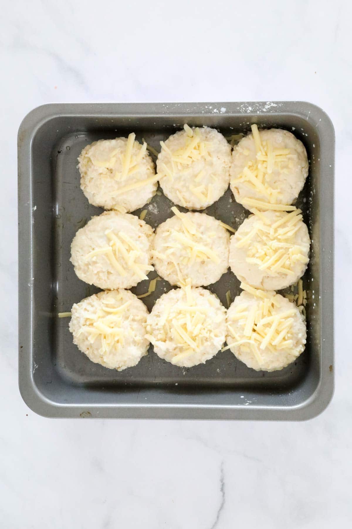 Cheese scones placed together in a square cake tin and sprinkled with a little grated cheese.