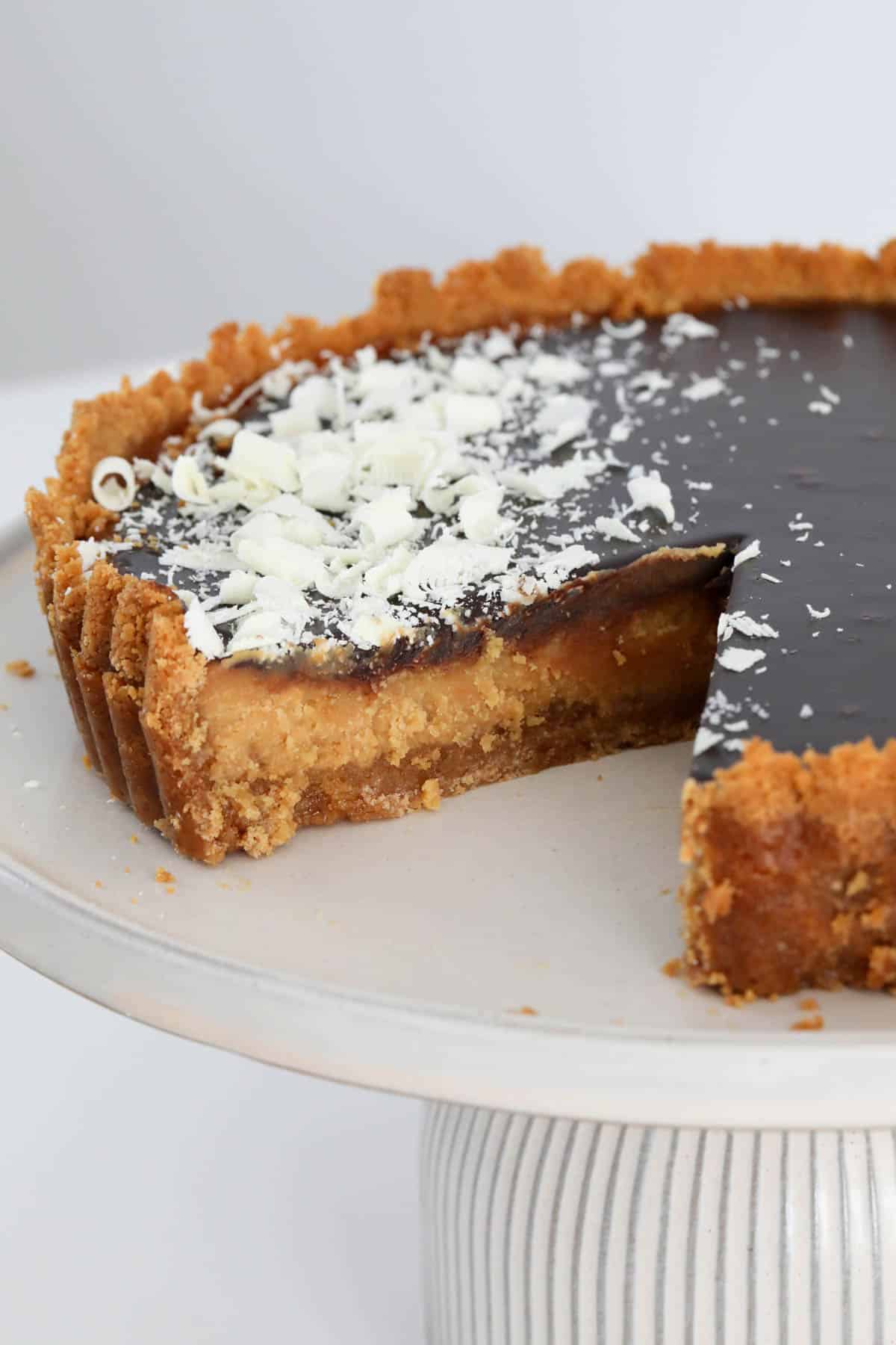 One slice removed from the tart showing the biscuit base, caramel filling and chocolate ganache on top.
