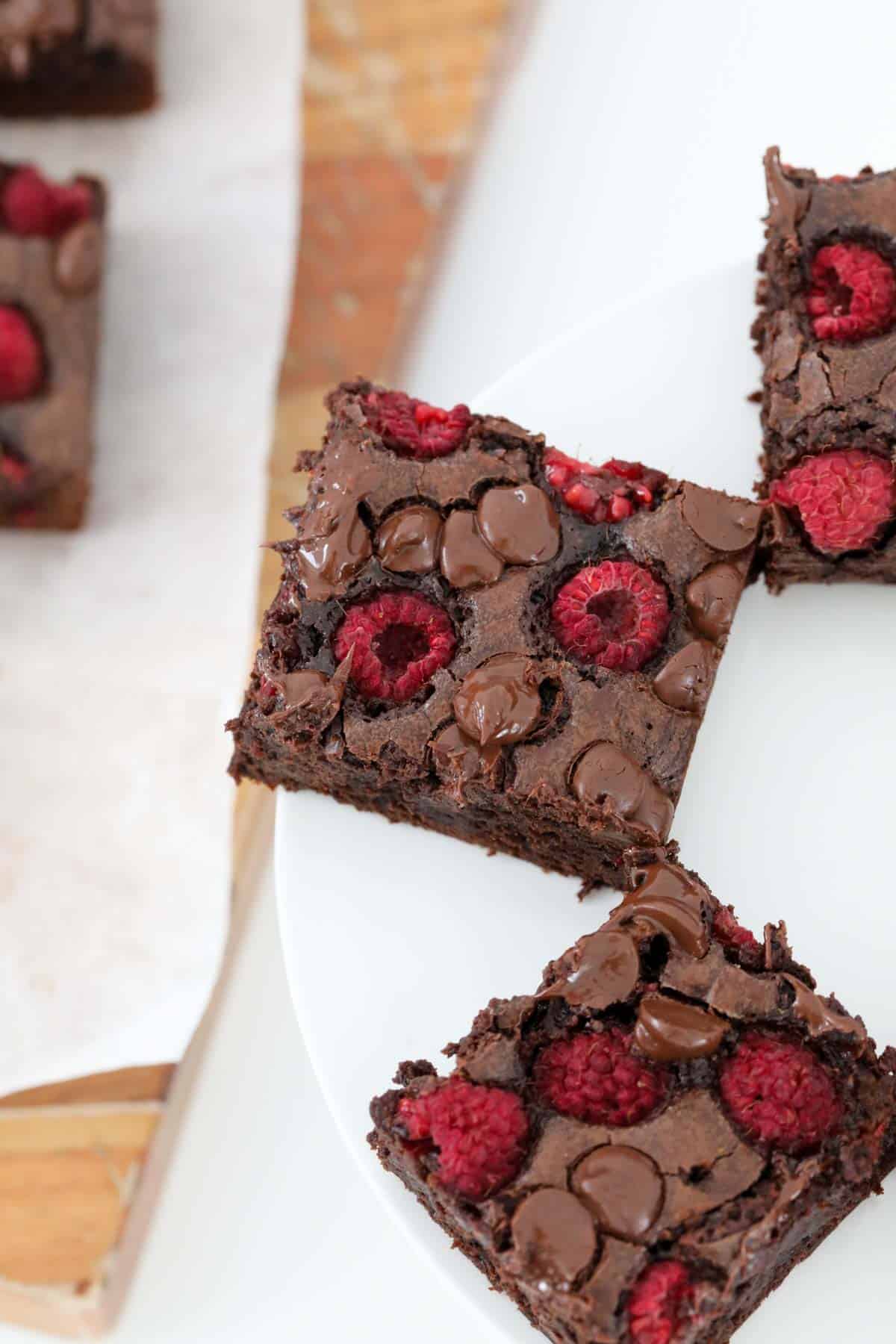 An overhead shot of brownie squares, dotted with raspberries and dark chocolate chips.