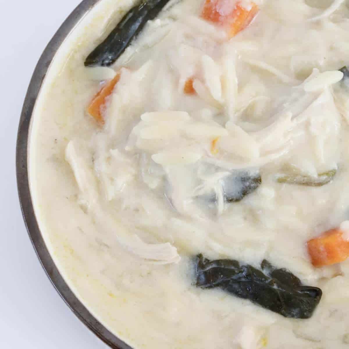 An overhead shot of a bowl of chicken, orzo, lemon spinach and carrot soup.