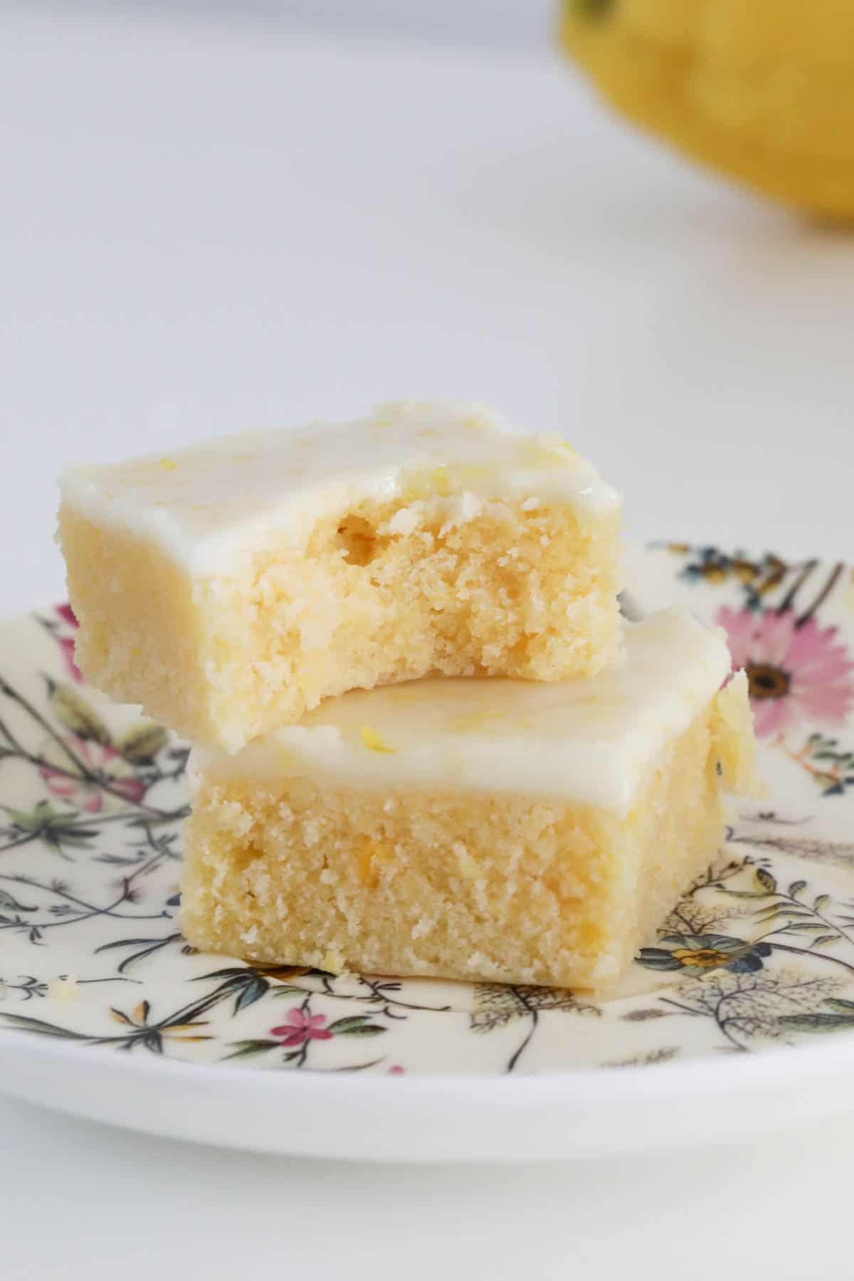 Two lemon blondies on a plate with a bite taken out of one.