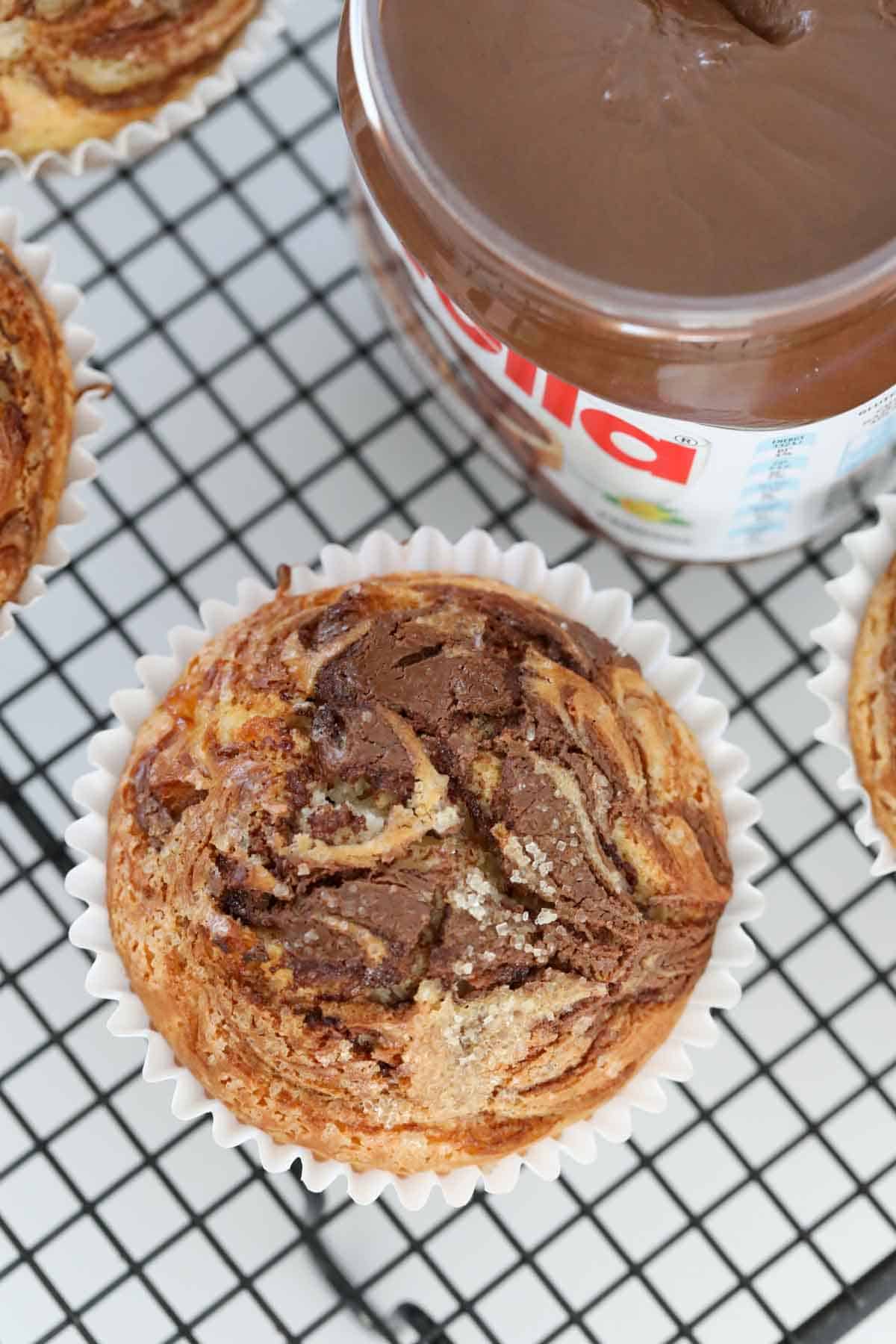 An overhead shot of a Nutella muffin with a jar of Nutella beside.