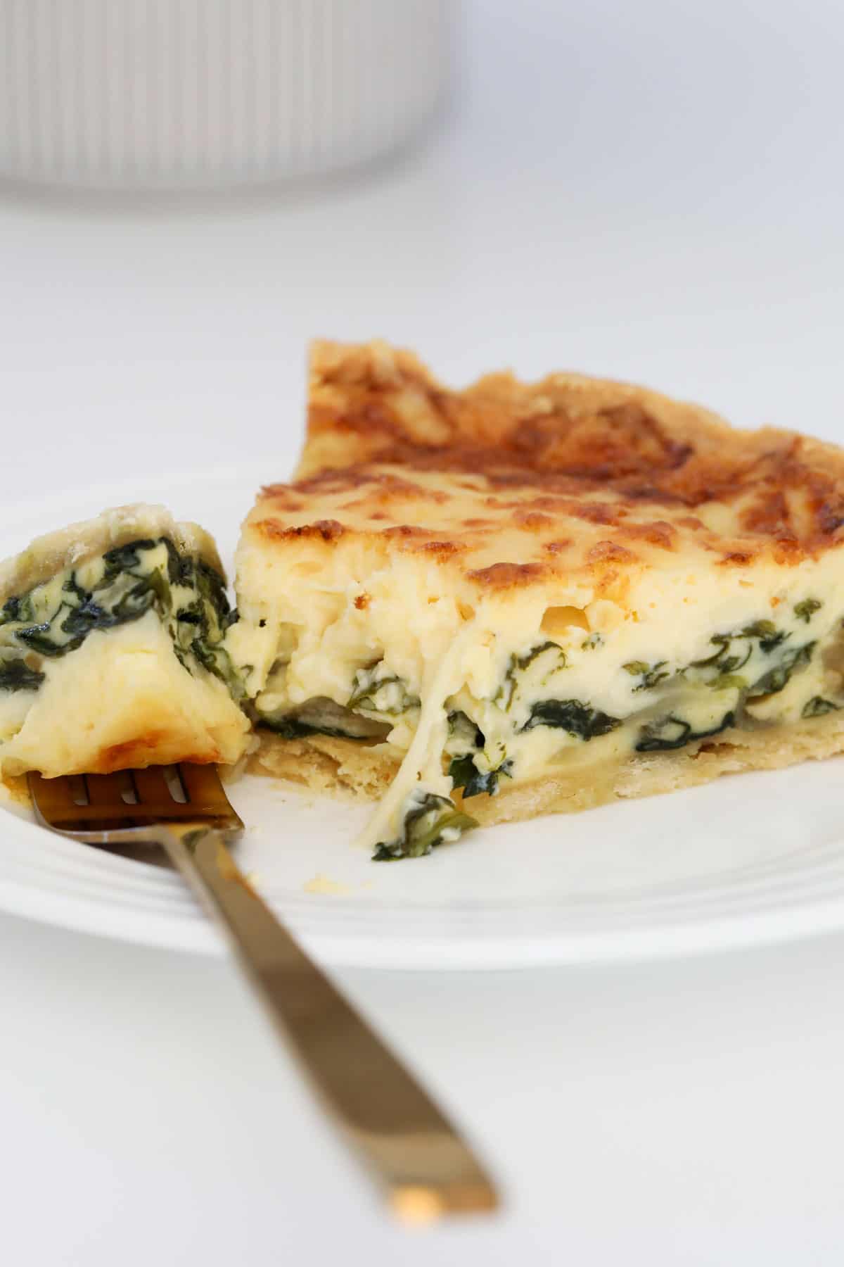 Spinach quiche on a plate with a gold fork resting on it.