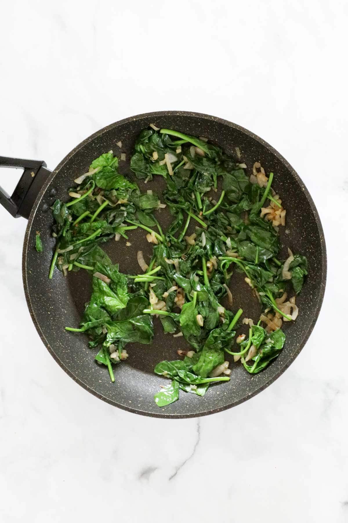 Spinach wilting in a frying pan with shallots.