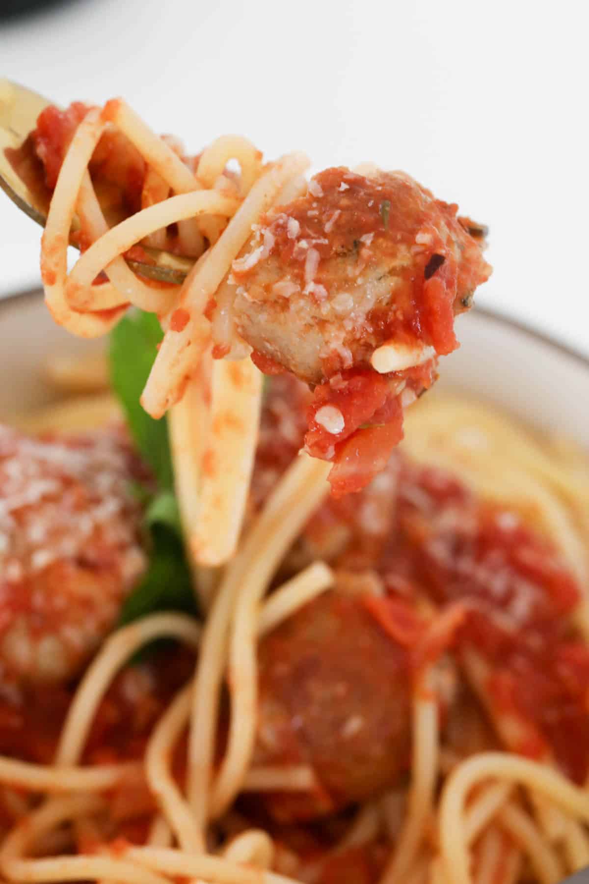 A fork holding a sausage meatball above a bowl.