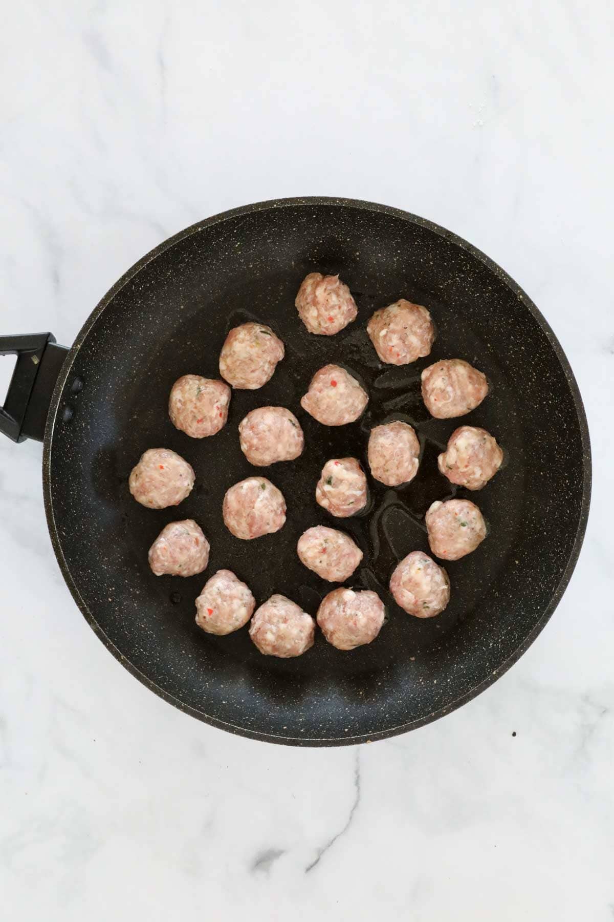 Meat from sausages rolled into meatballs, and placed in a frying pan.