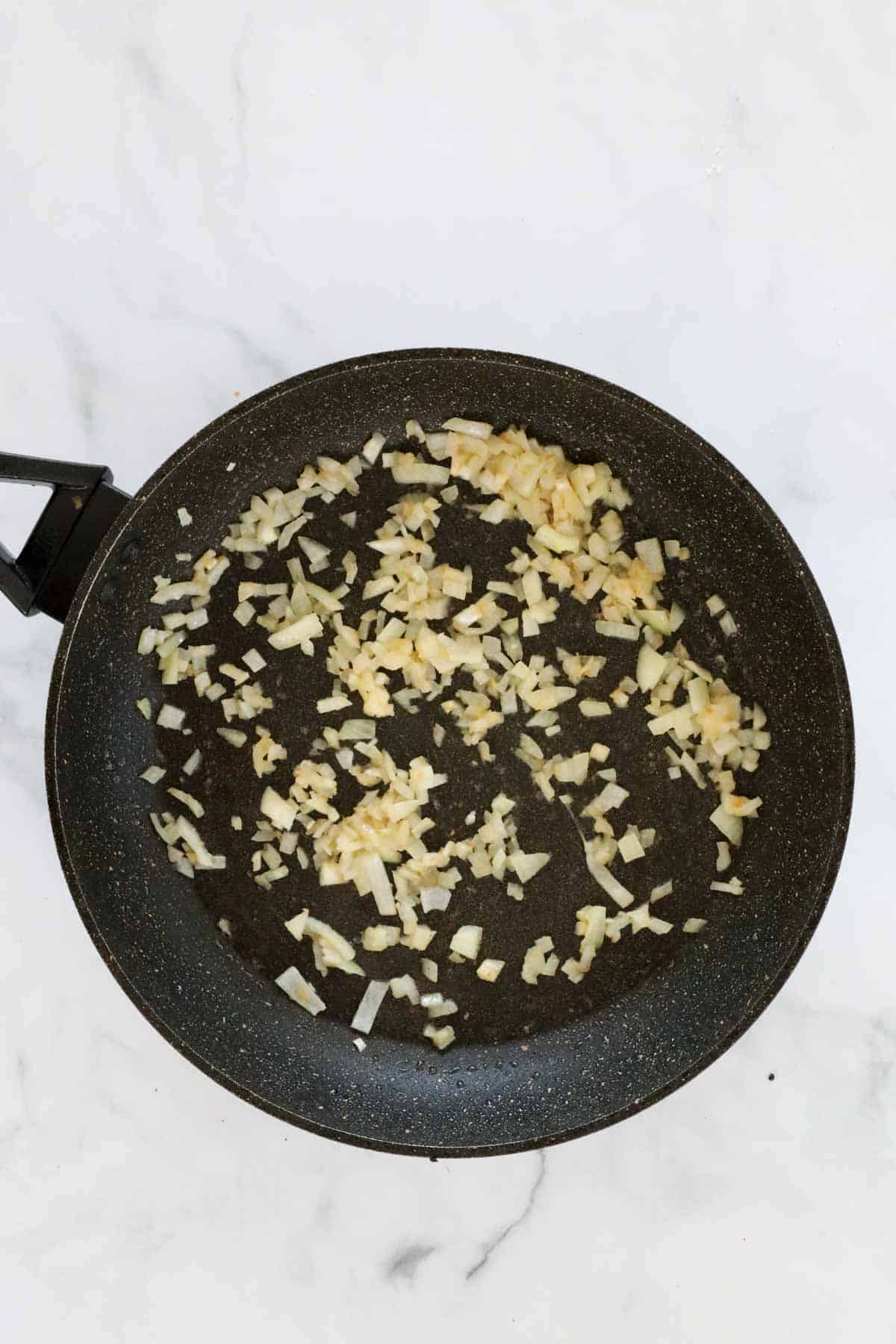 Garlic and diced onion sauteing in a frying pan.