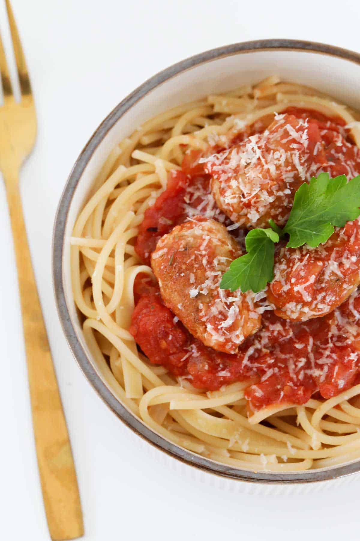 Sausage meatballs in a tomato sauce, in a bowl filled with spaghetti noodles.