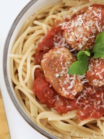 A pile of Italian sausage meatballs cooked in a tomato sauce, served on a bowl of spaghetti pasta.