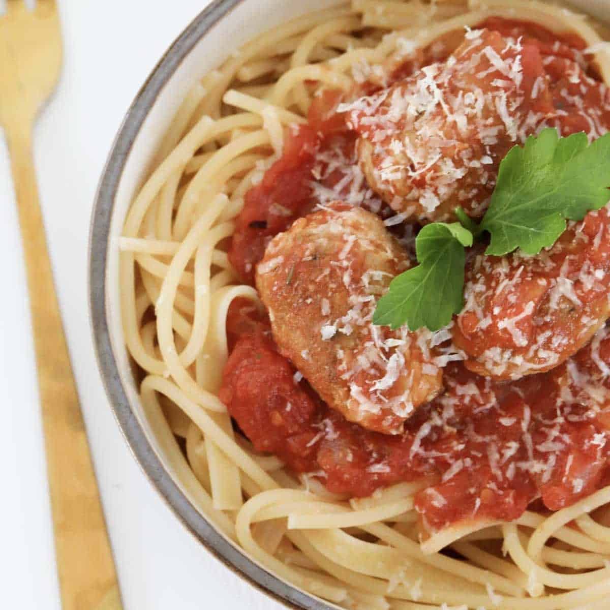 A pile of Italian sausage meatballs cooked in a tomato sauce, served on a bowl of spaghetti pasta.