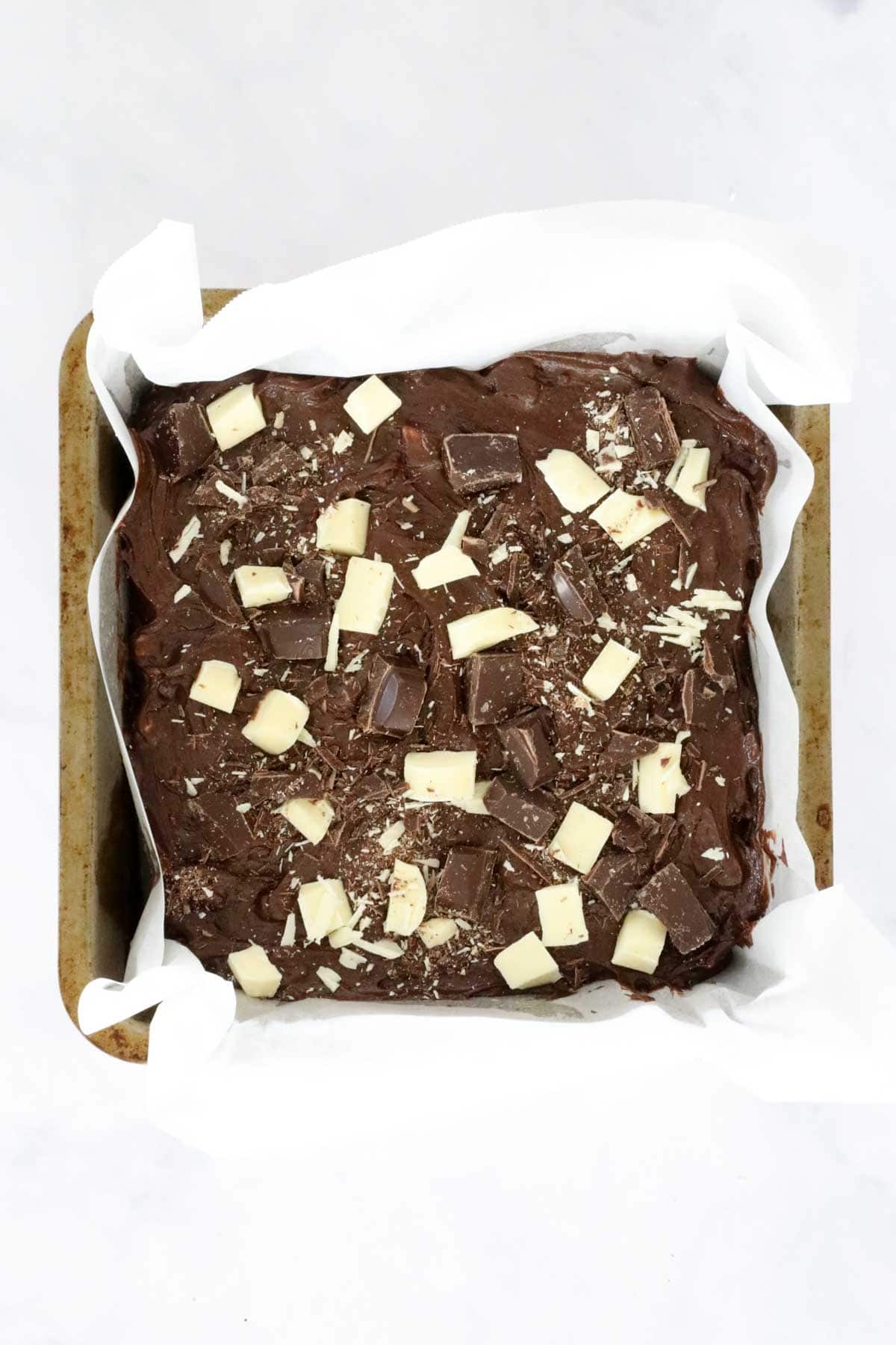 Triple chocolate brownie mix in baking tin, studded with chunks of chocolate.