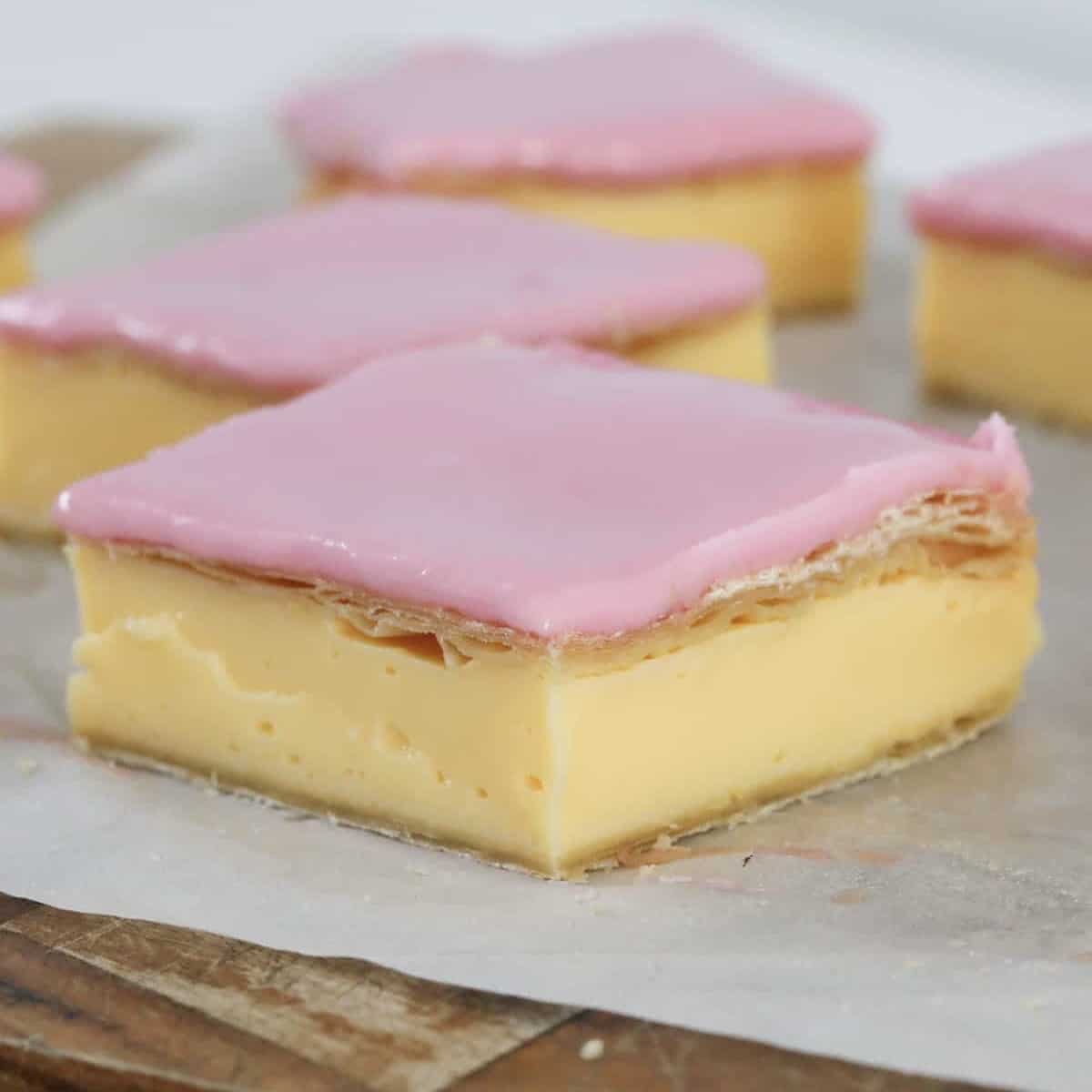 Pieces of homemade vanilla custard slice with pink icing.