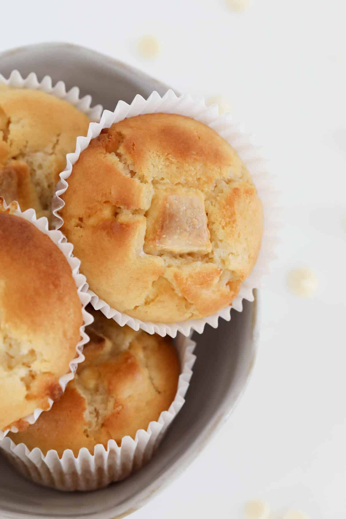 A bowl full of muffins with chunks of white chocolate on top.