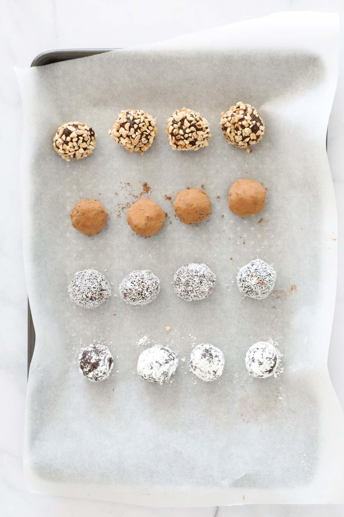 Four different varieties of coated truffles on a baking paper lined tray.