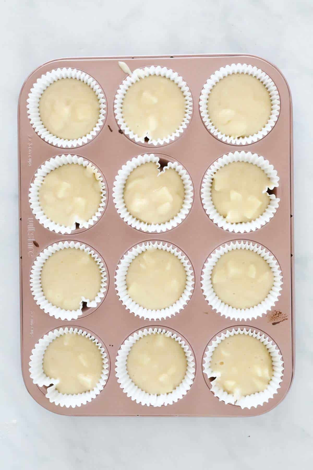 Muffin cases half filled with batter and chunks of white chocolate.