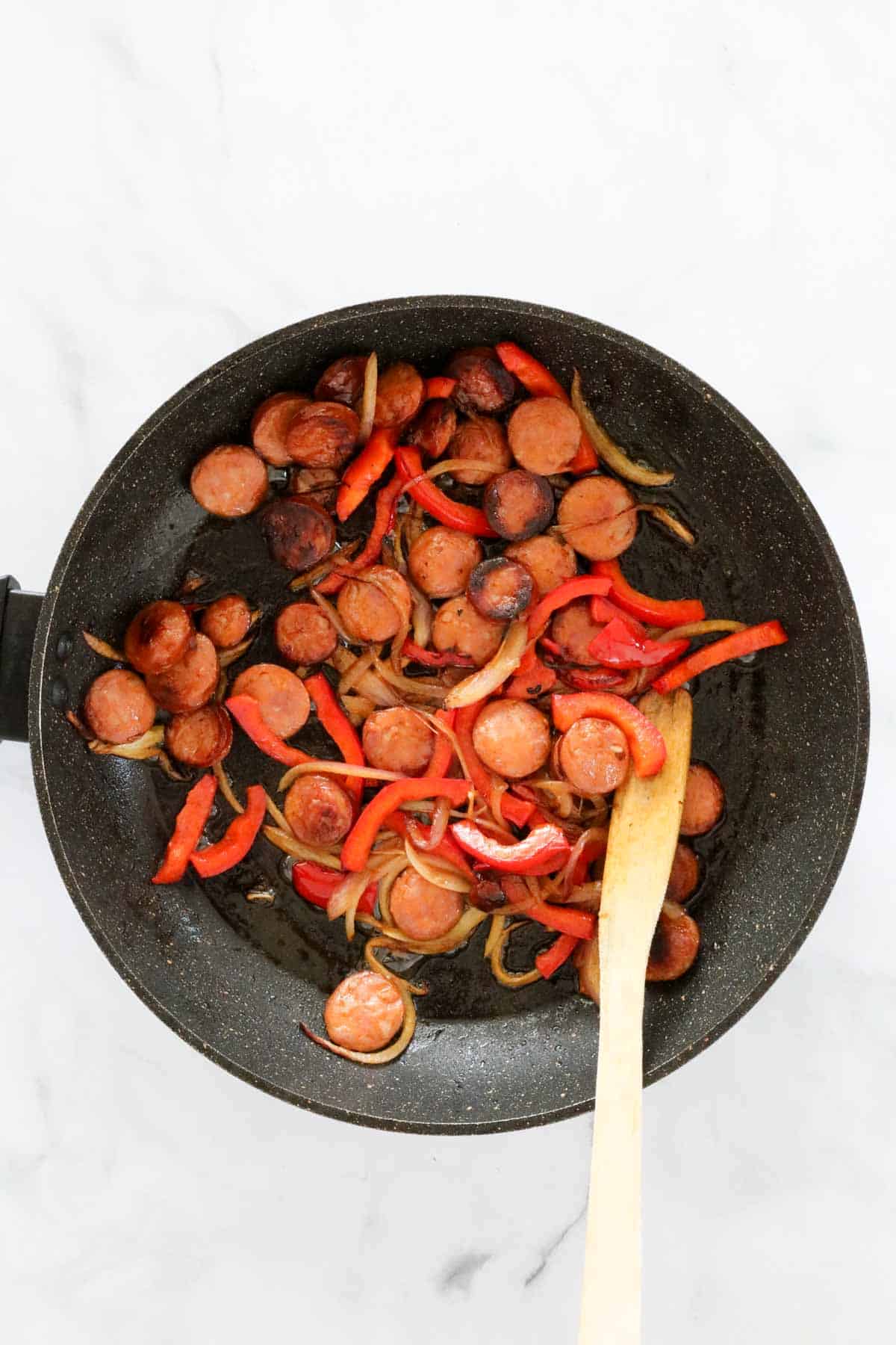 Spicy sausage, red onion and red capsicum in a frying pan.