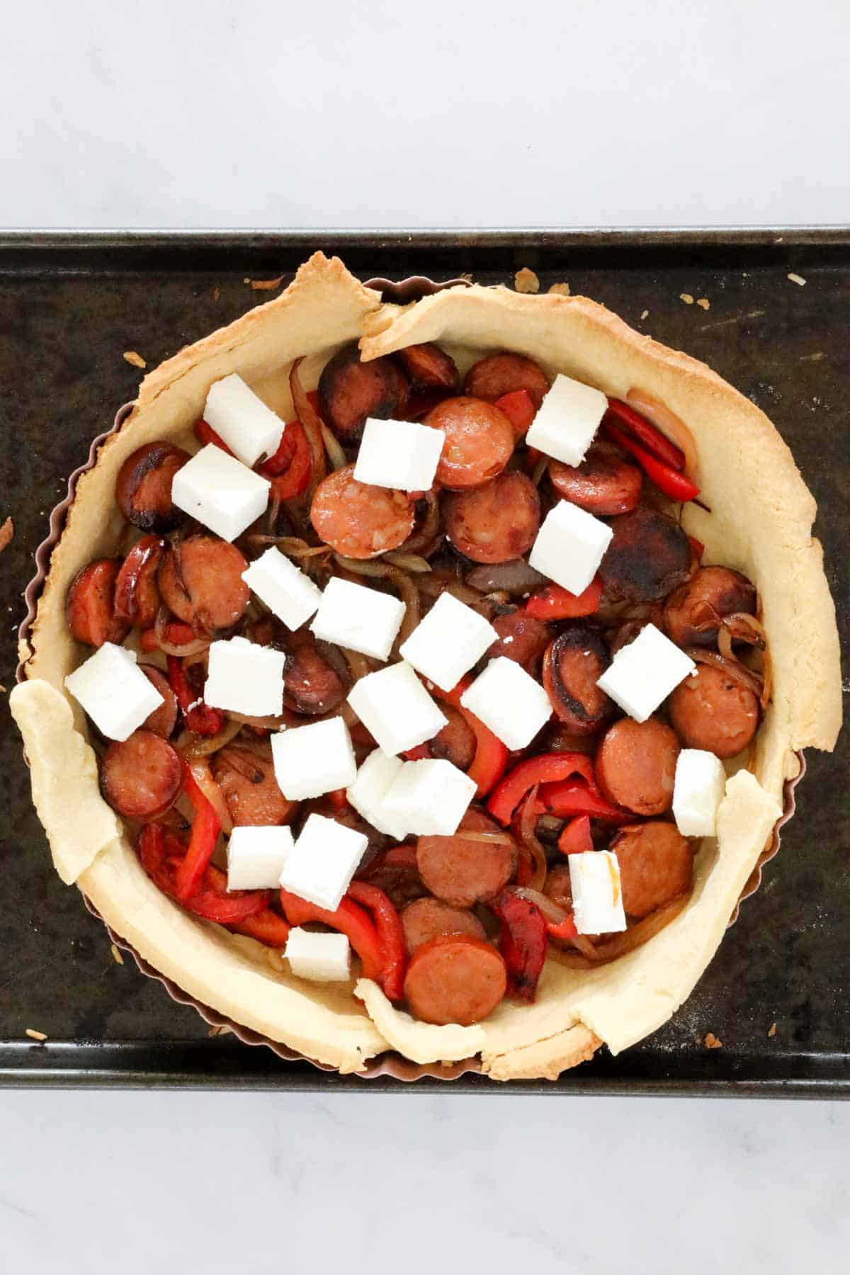 The cooked chorizo and vegetables placed in the pastry shell, topped with cubes of feta cheese.