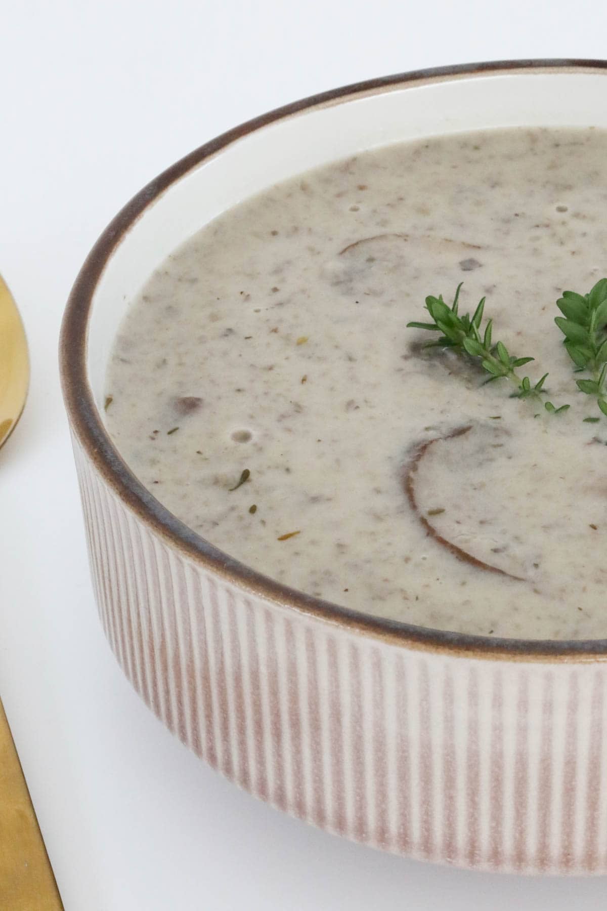 Side view of creamy mushroom soup served topped with fresh thyme.