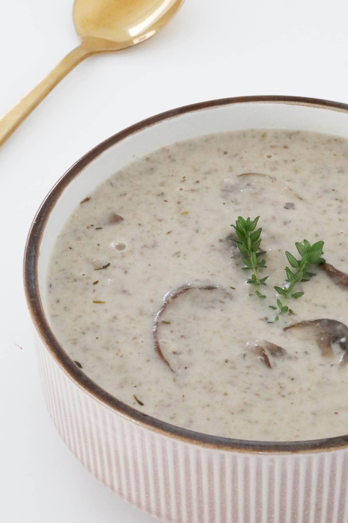 Creamy mushroom soup in a bowl topped with fresh thyme.