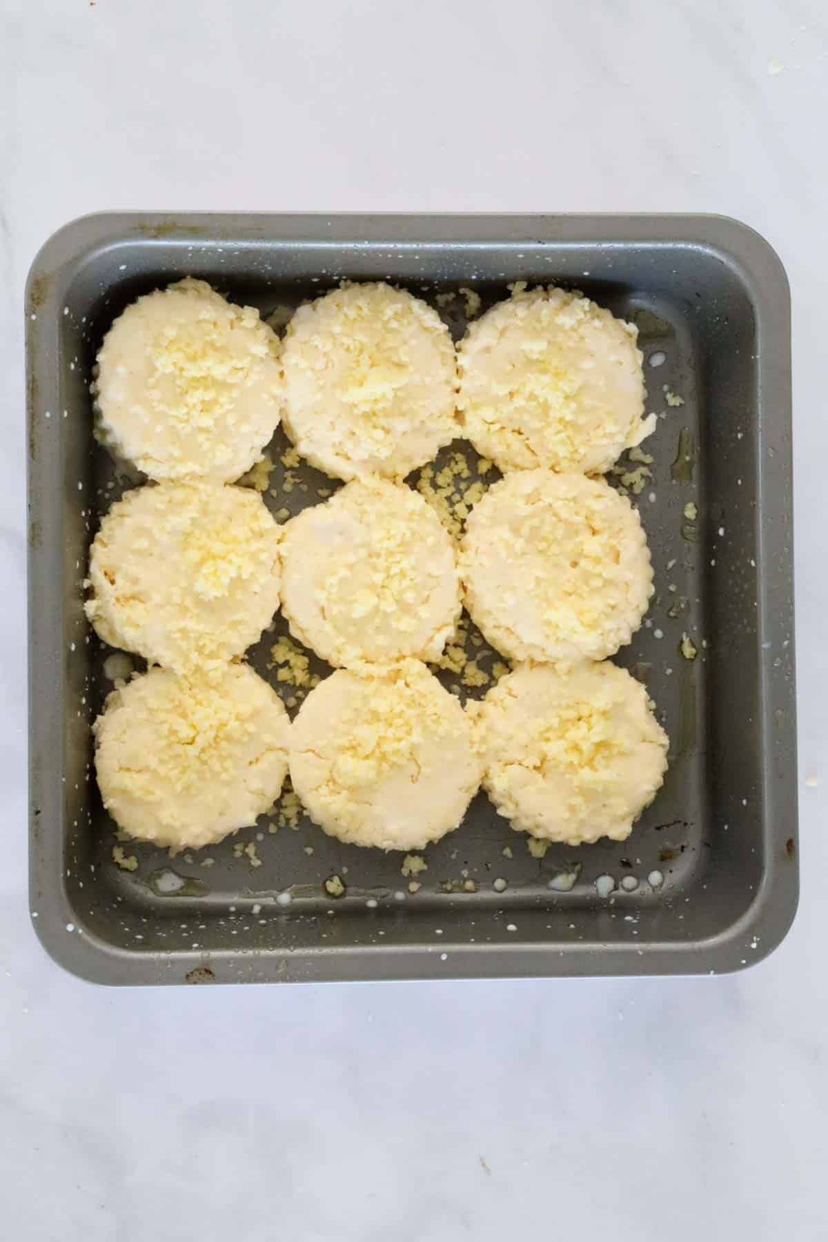 Scones placed in a baking tin and sprinkled with grated cheddar.